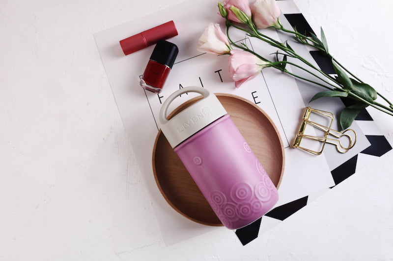 Pink and white container on a magazine with flowers and nail polish nearby